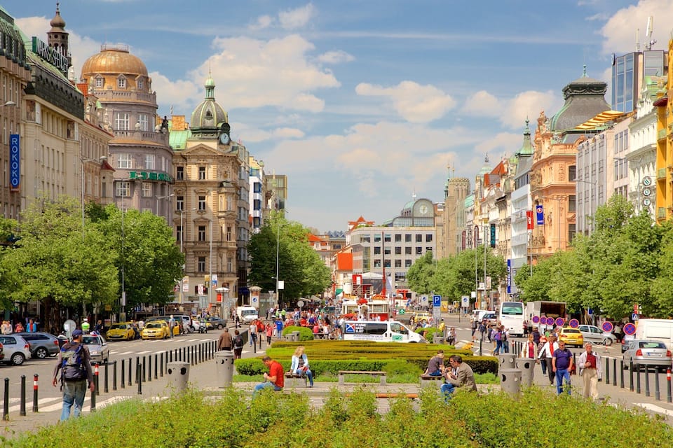 Vivace via cittadina con edifici storici, una piazza centrale affollata e un tram.