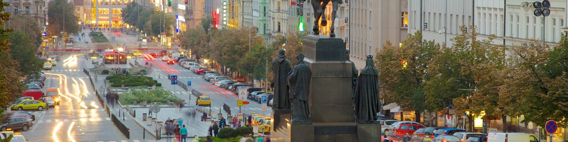 A busy city street with a statue of a man on horseback, surrounded by historic buildings and a tram line.