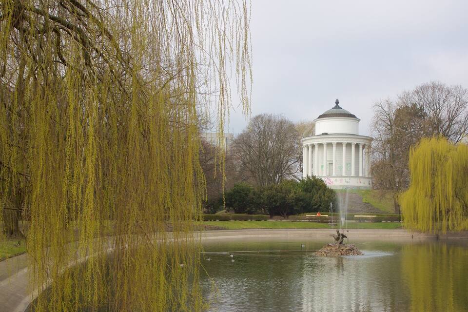 Un saule pleureur, une fontaine et un bâtiment blanc orné de colonnes.