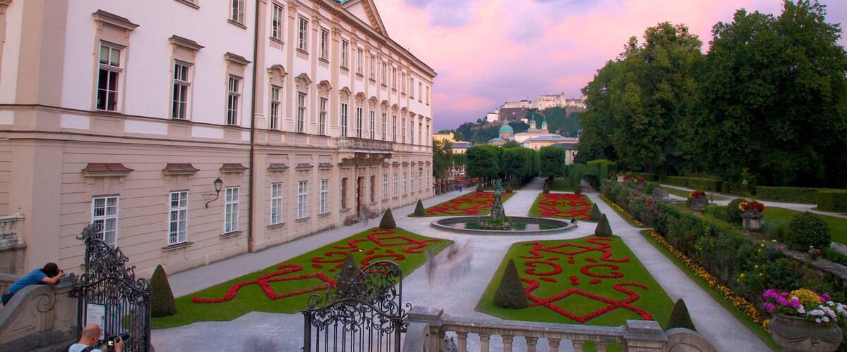 A grand building with a formal garden, including geometric flower beds and a fountain.