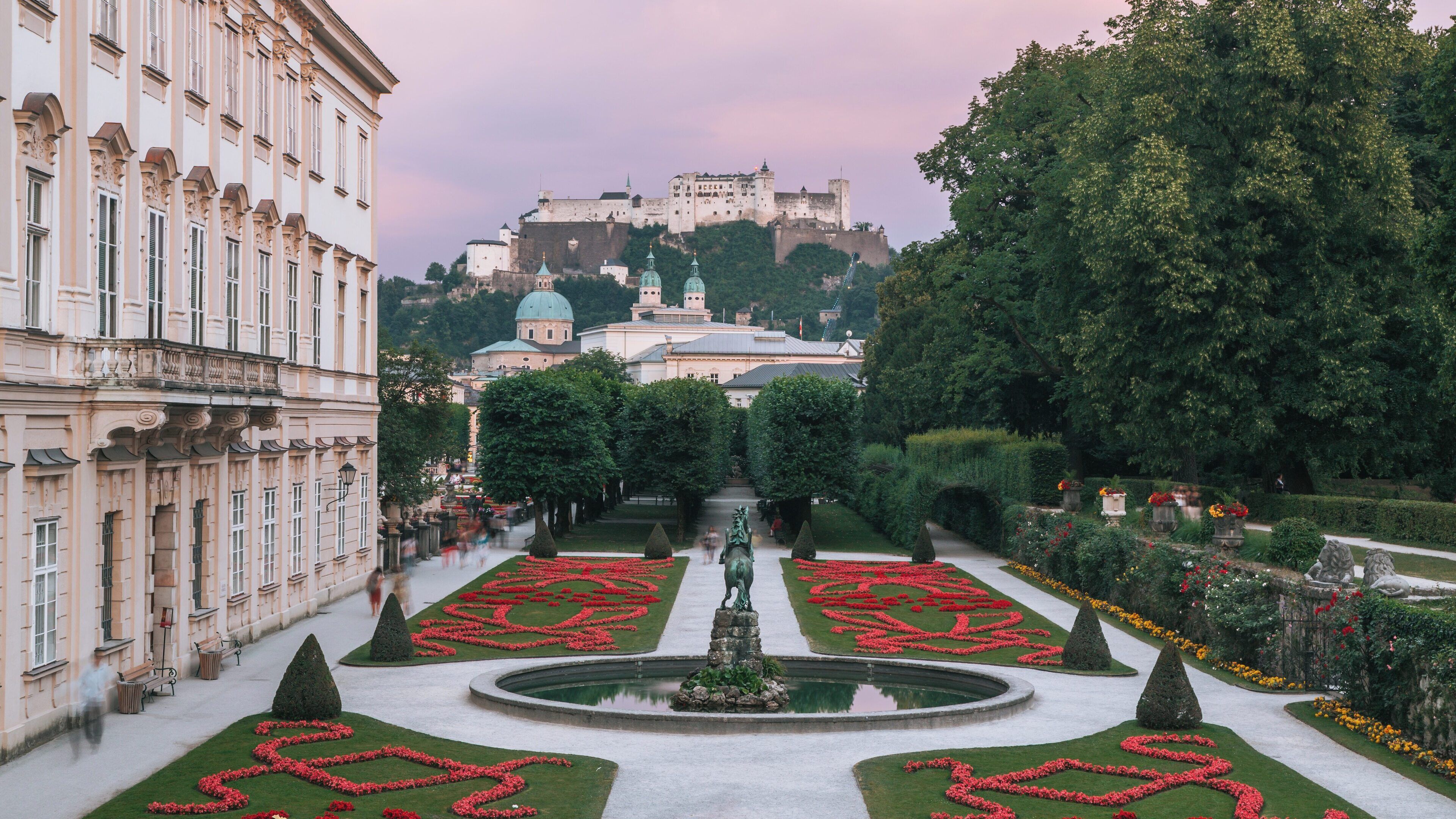 Magnificent Mirabell Palace and Gardens showcase stunning floral designs with Hohensalzburg Fortress in the background during a serene sunset in Salzburg