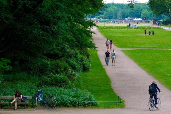 Ein Park mit befestigtem Weg, viel Grün, einem Fahrrad und Fußgängern.