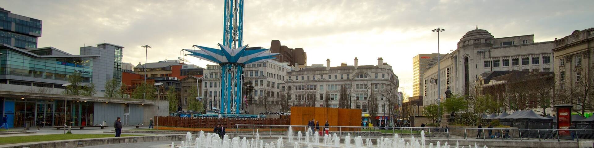 A city square with a fountain, a tall blue structure, and historic buildings.