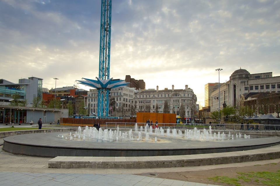 A city square with a fountain, a tall blue structure, and historic buildings.