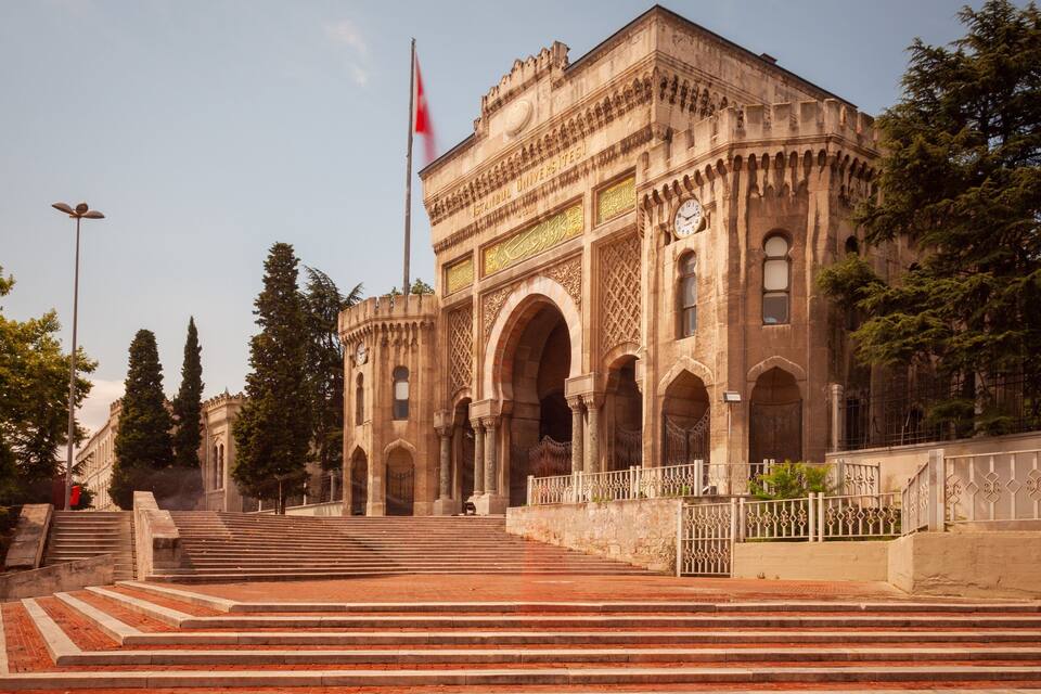 A historic building with intricate architecture, a flag, and a staircase leading up to it.