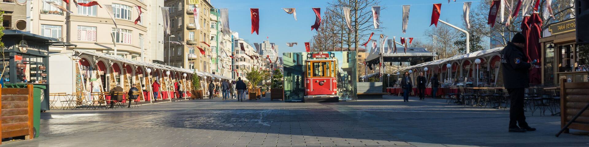 A tram in a city square with buildings and flags.