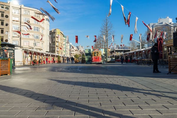 Eine Stadtbahn auf einem Stadtplatz, umgeben von Gebäuden und Flaggen.
