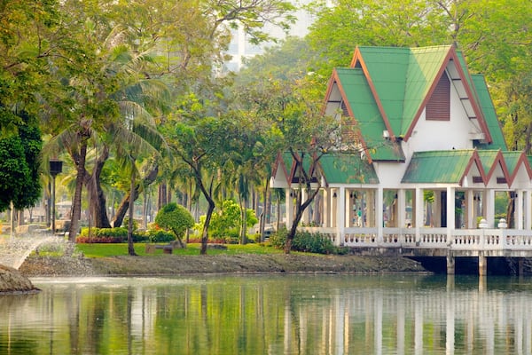 Ein traditionelles thailändisches Haus mit einem grünen Dach, umgeben von üppiger Vegetation und einem ruhigen See.