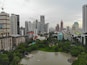 A cityscape with high-rise buildings, a large body of water, and a park with a traditional pavilion.