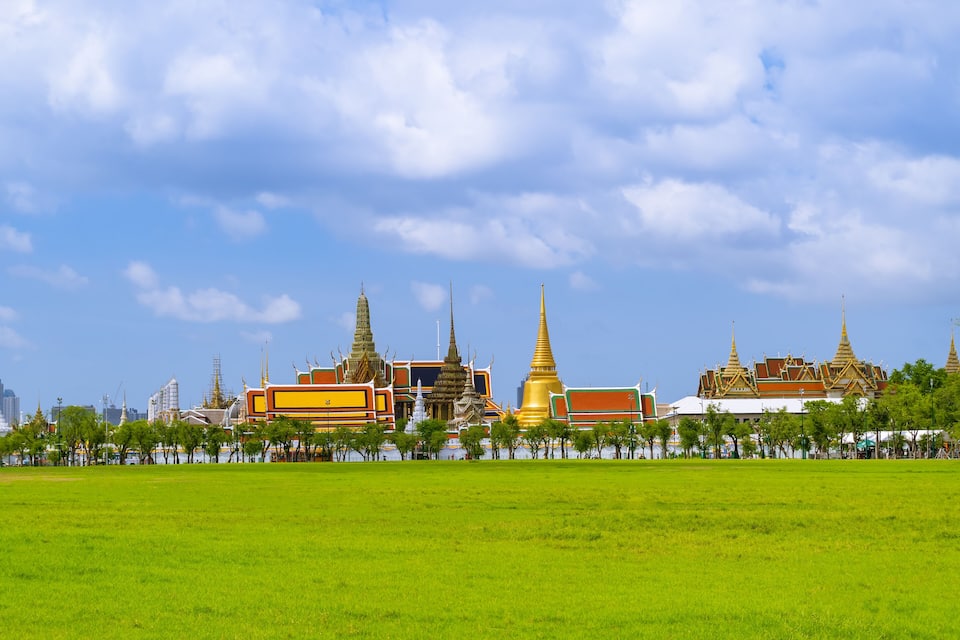 A large green field with traditional Thai temples and buildings in the background.