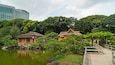 A traditional Japanese garden with a wooden bridge, a pond, and buildings with thatched roofs.
