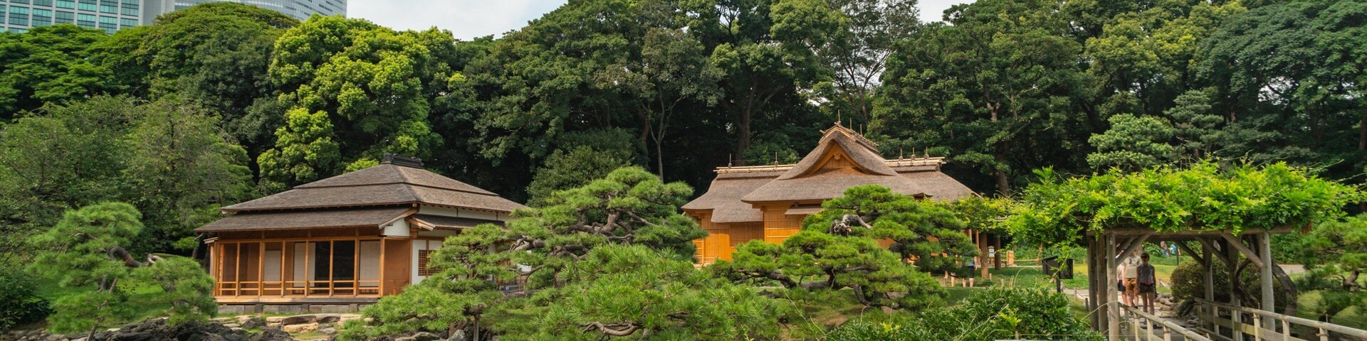 Um jardim japonês tradicional com uma ponte de madeira, um lago e construções com telhados de palha.