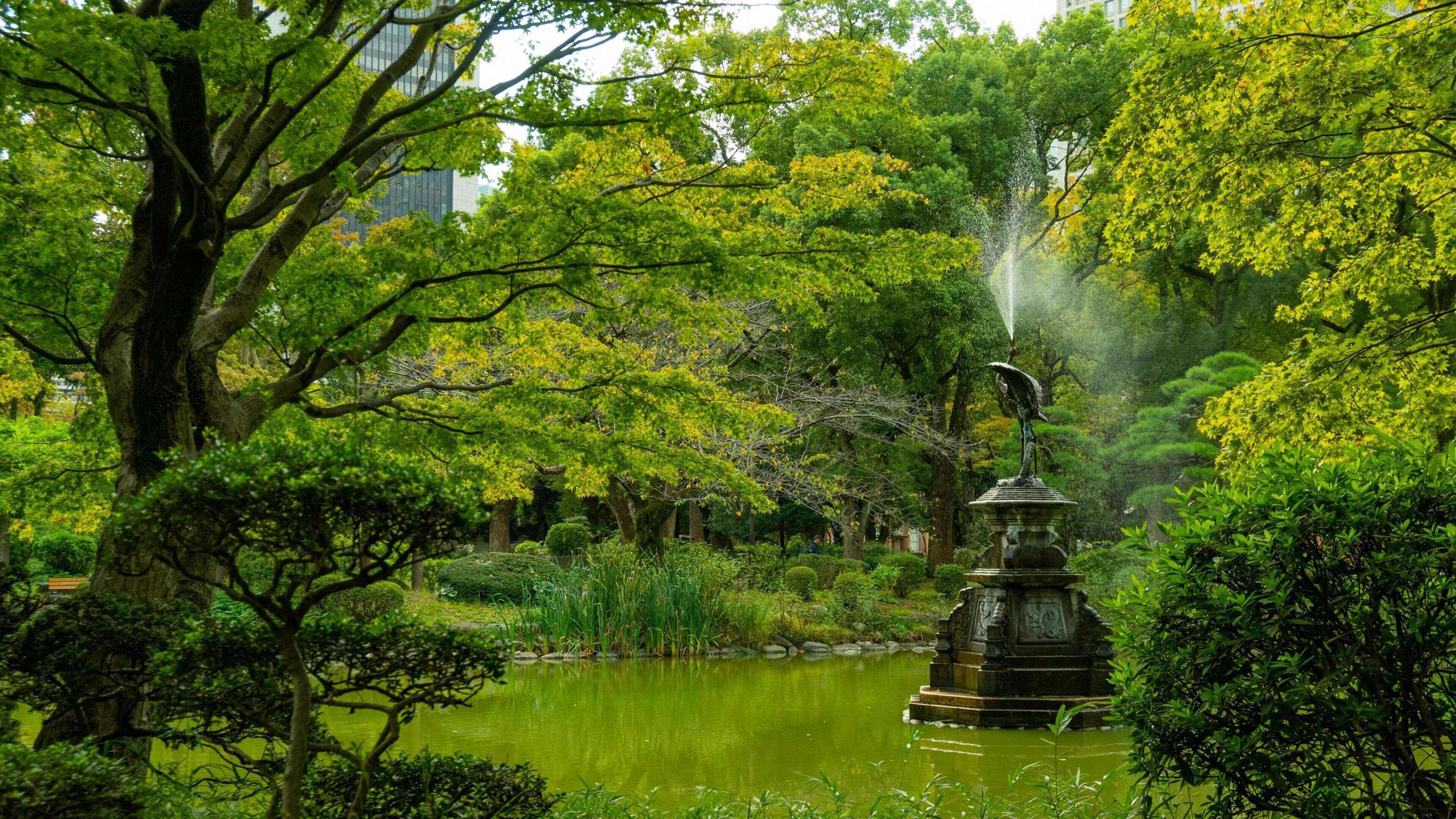 Un jardín tranquilo con un estanque, abundante vegetación y una estatua de fuente.