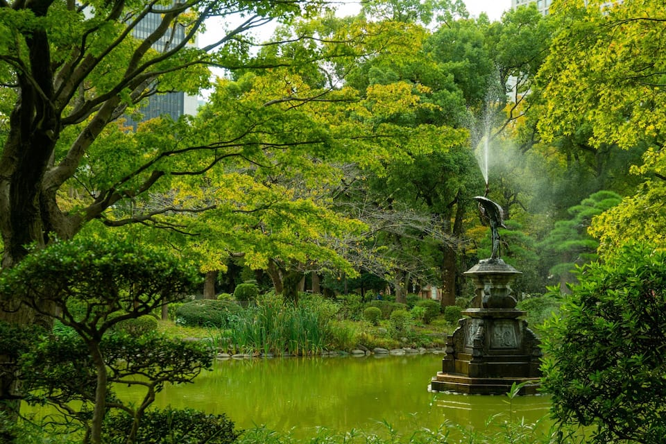 A tranquil garden with a pond, lush greenery, and a fountain statue.