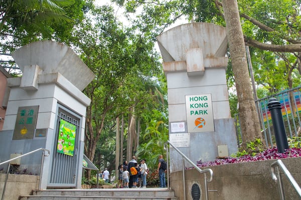A gate with a sign reading "Hong Kong Park" surrounded by lush greenery and trees.