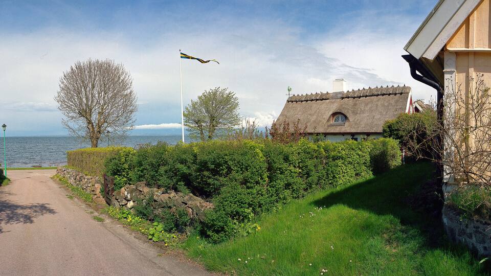A narrow path beside a lake, a thatched-roof house, and a flagpole with a flag.