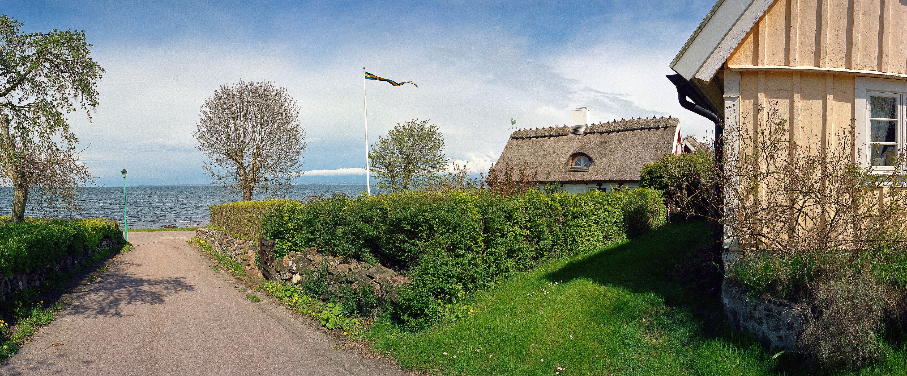 A narrow path beside a lake, a thatched-roof house, and a flagpole with a flag.