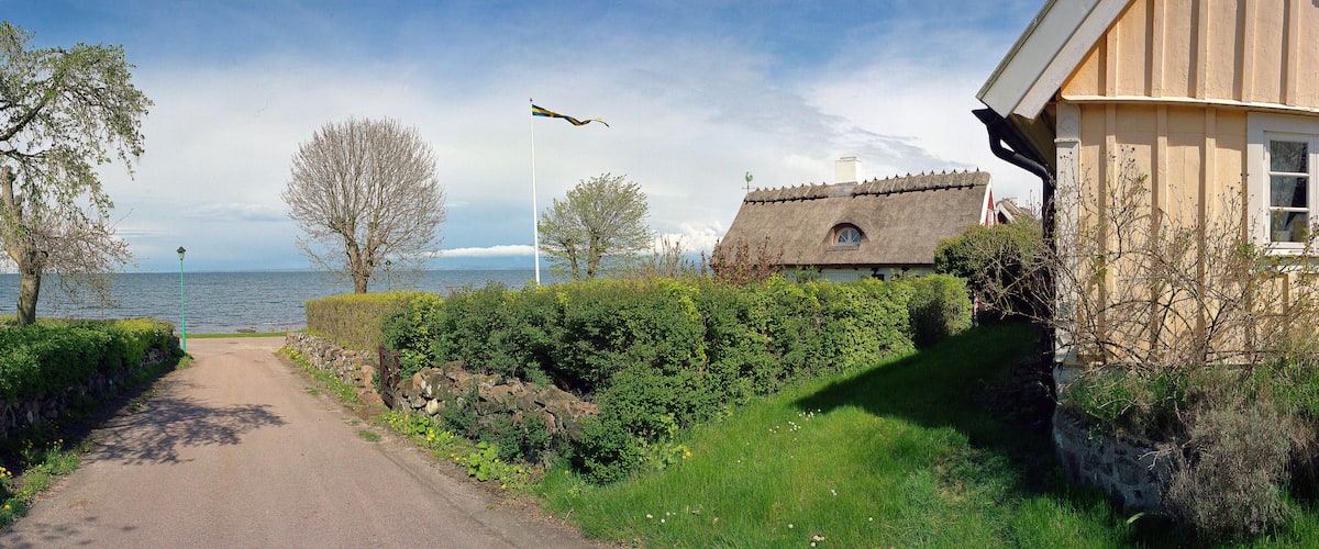 A narrow path beside a lake, a thatched-roof house, and a flagpole with a flag.