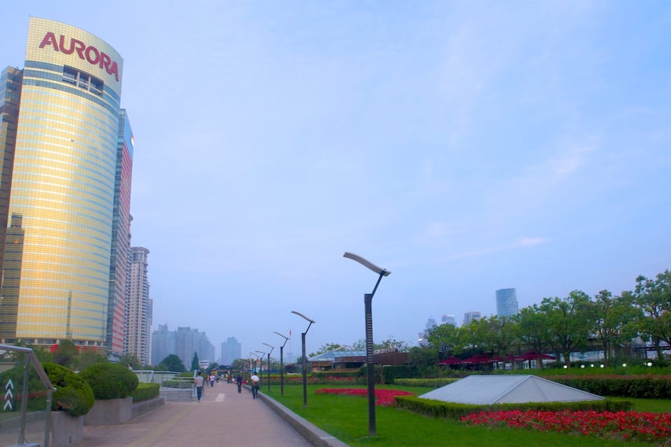 A cityscape with a prominent AUORA building, a pedestrian pathway, and a park with red flowers.
