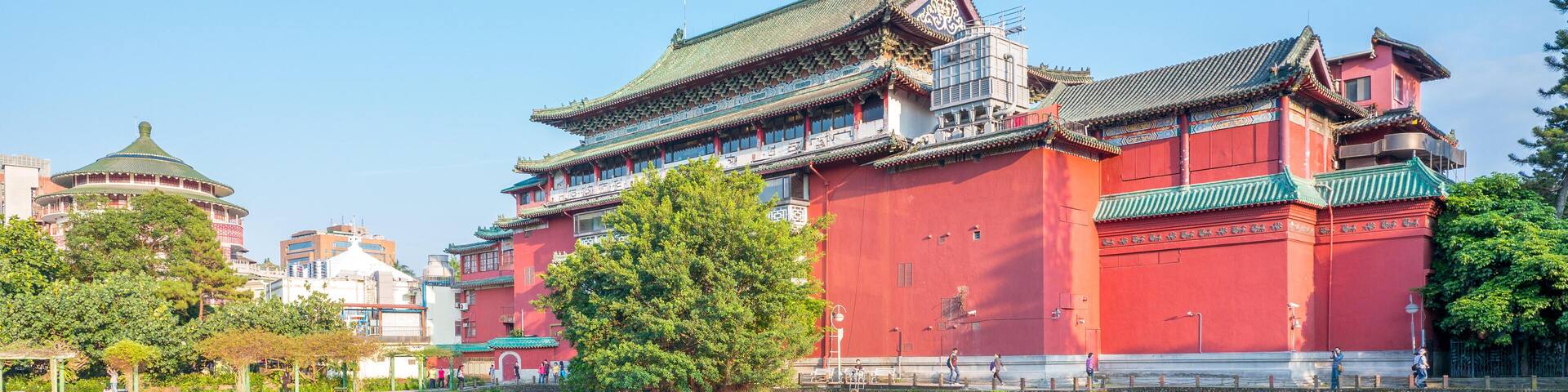 A traditional red building with a green roof, reflecting in a calm body of water.