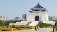 A traditional Chinese-style pavilion with a blue roof and white walls, surrounded by well-maintained gardens and a cityscape in the background.