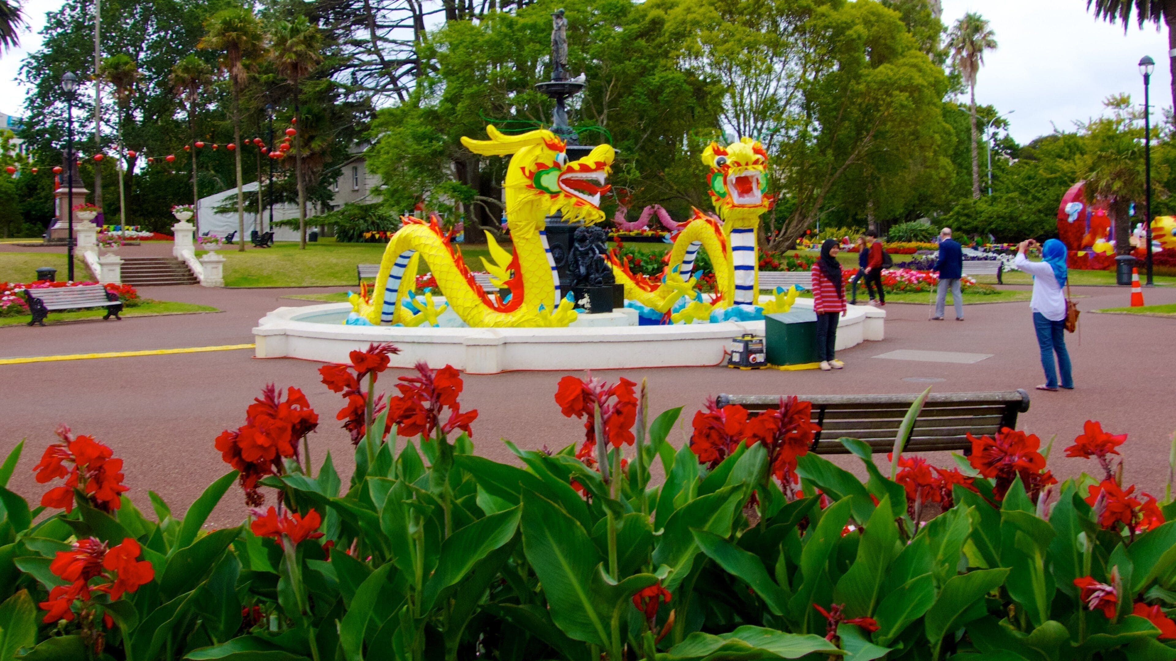 A dragon sculpture in a park with red flowers in the foreground.
