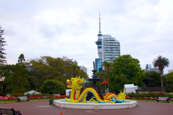 A park with a dragon statue, benches, and a tall building in the background.