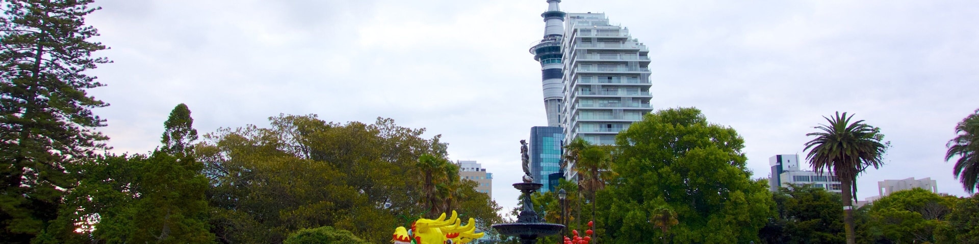Un parque con una estatua de dragón, bancos y un edificio alto al fondo.