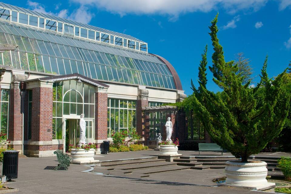 A greenhouse with a glass roof, brick walls, and a statue in front.