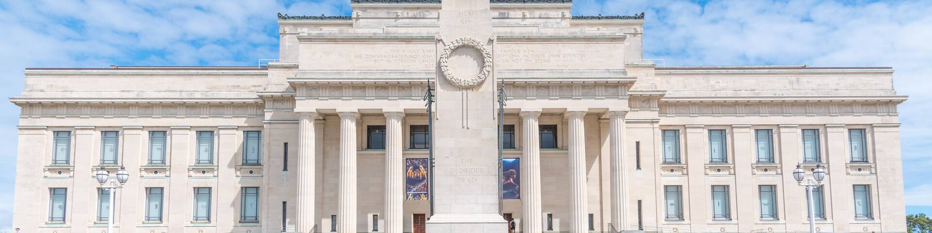 A large neoclassical building with a central monument, wide steps leading to the entrance, and banners on the facade.