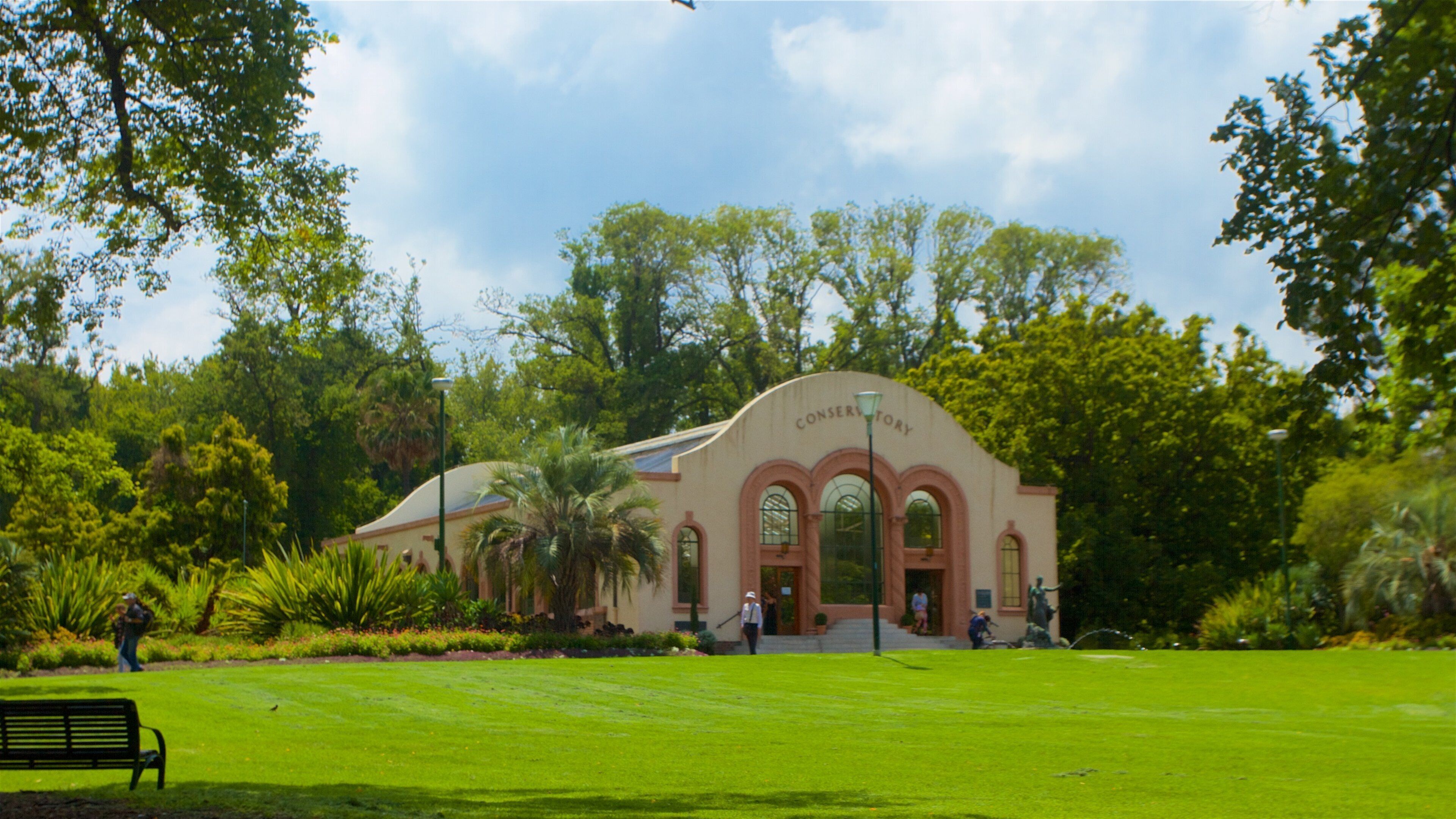 A conservatory with arched windows and a sign, surrounded by lush greenery and a well-maintained lawn.