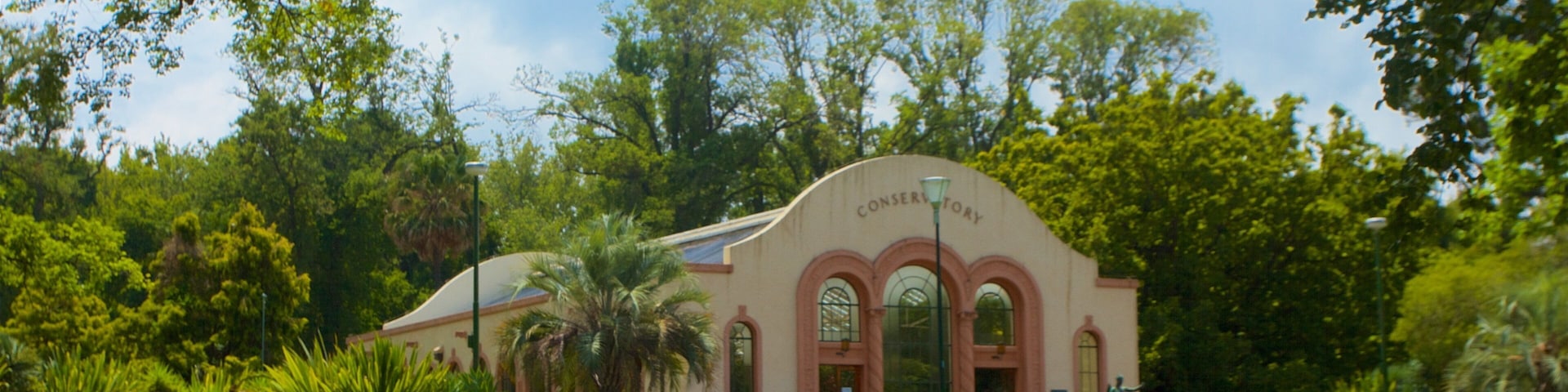 A conservatory with arched windows and a sign, surrounded by lush greenery and a well-maintained lawn.