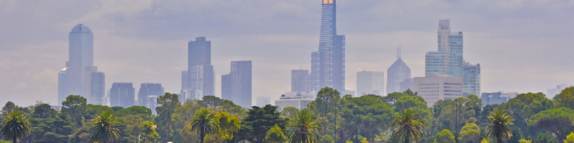 Melbourne city skyline under gathering storm clouds with Albert Park Lake in the foreground and the Eureka Skydeck 88 building being prominent.