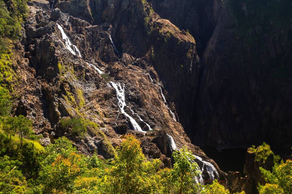 A multi-tiered waterfall cascading down a rocky cliff surrounded by lush greenery.