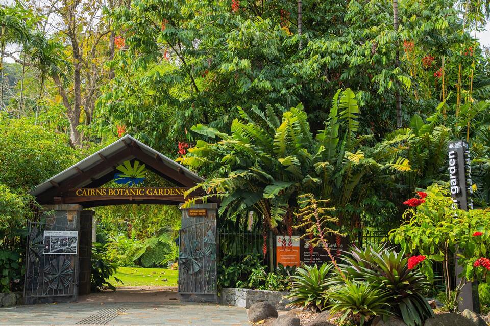 La entrada a los Jardines Botánicos de Cairns, con un cartel, abundante vegetación y un sendero de piedra.