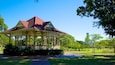 A gazebo with a red roof and white columns in a park with green trees and a clear sky.