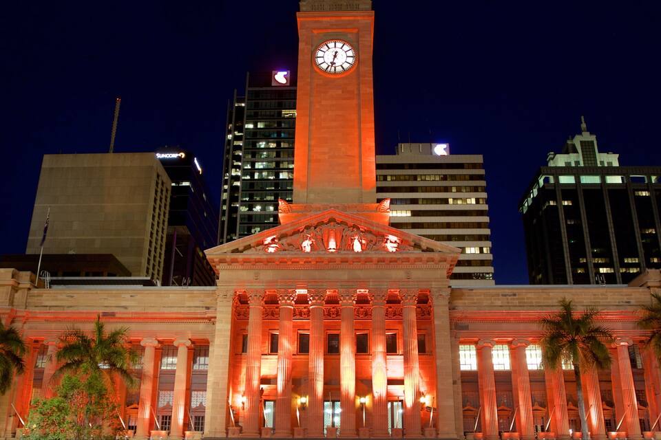 A historic building with a clock tower, palm trees, and modern skyscrapers in the background.