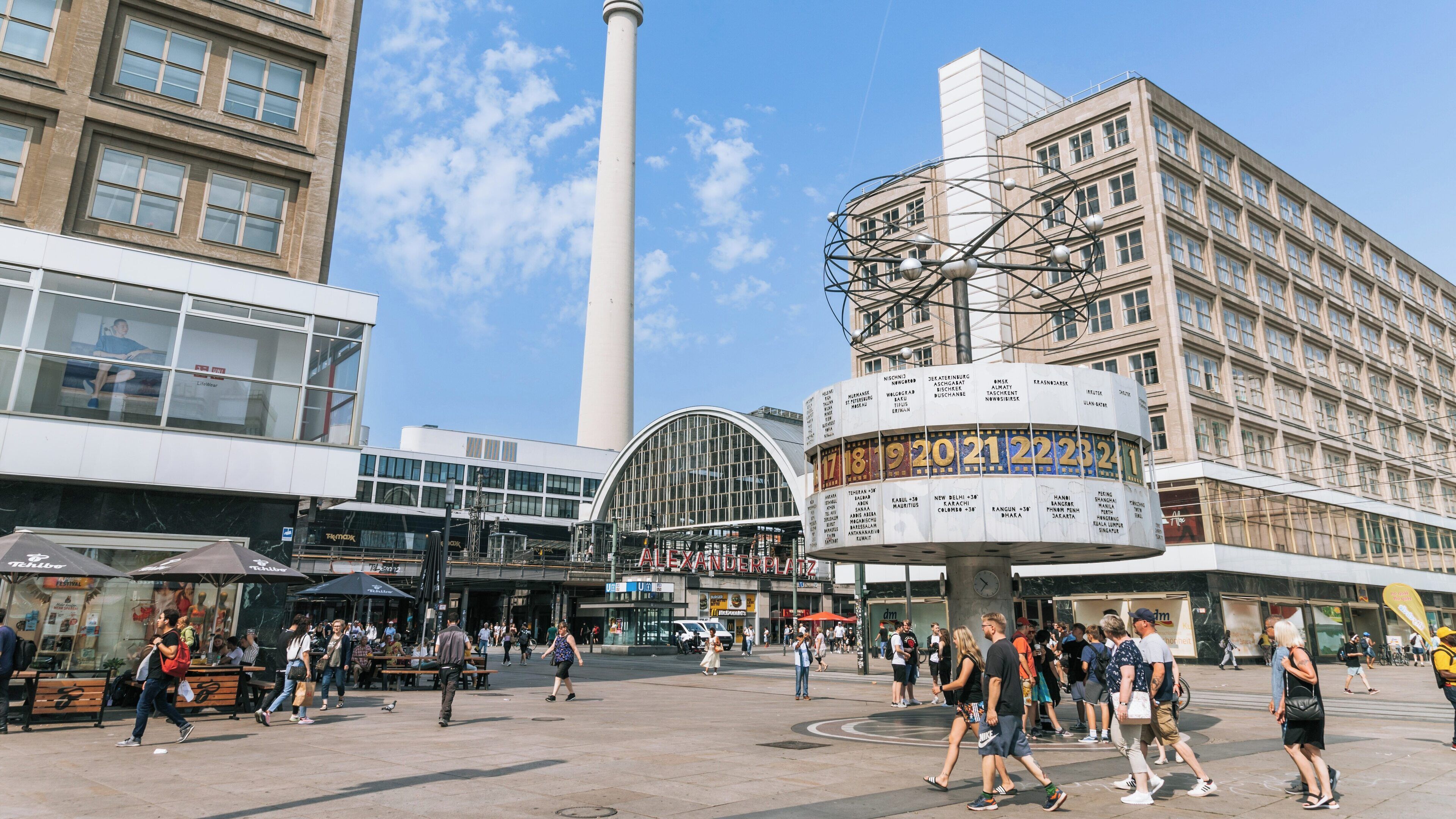 Vibrant atmosphere at Alexanderplatz in Mitte, Berlin, bustling with visitors and marked by iconic landmarks and modern architecture under a clear blue sky