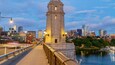 Une vue sur les toits d’une ville, avec une tour imposante, une rivière et un pont éclairé par des lampadaires.