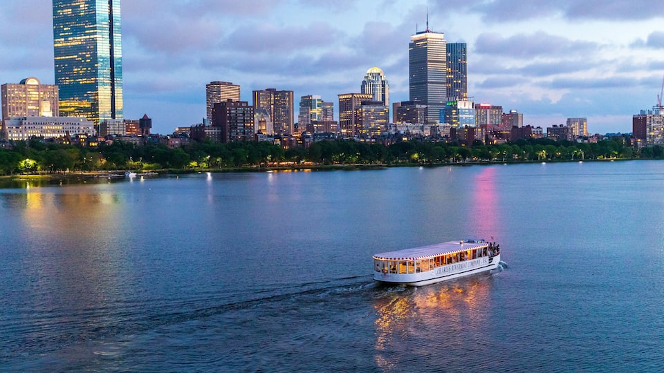 A river with a boat, a city skyline with modern buildings, and a park with trees along the riverbank.
