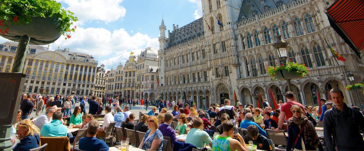 A bustling square with ornate buildings, outdoor seating, and a crowd of people.