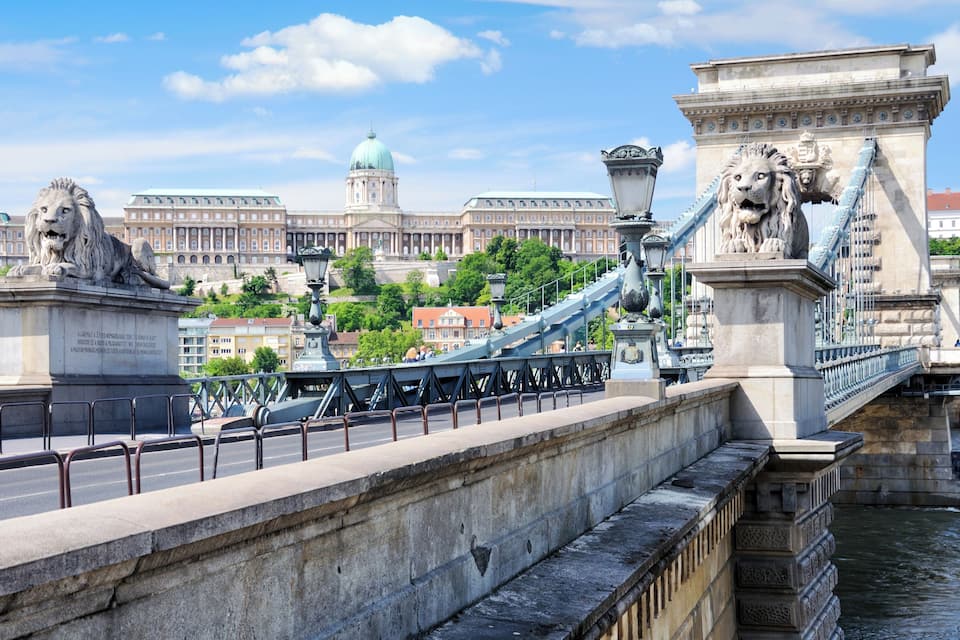 A bridge with lion statues, a large building with a dome, and a river.