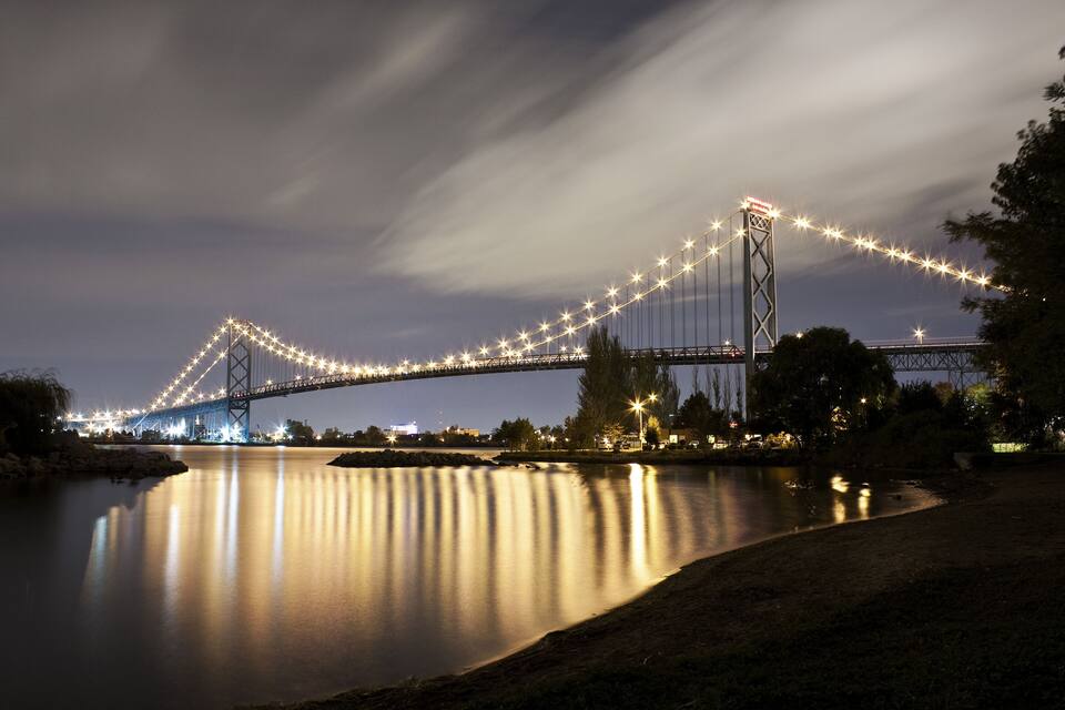 Ein Nachtblick auf eine große Hängebrücke, deren Lichter sich im Wasser spiegeln.