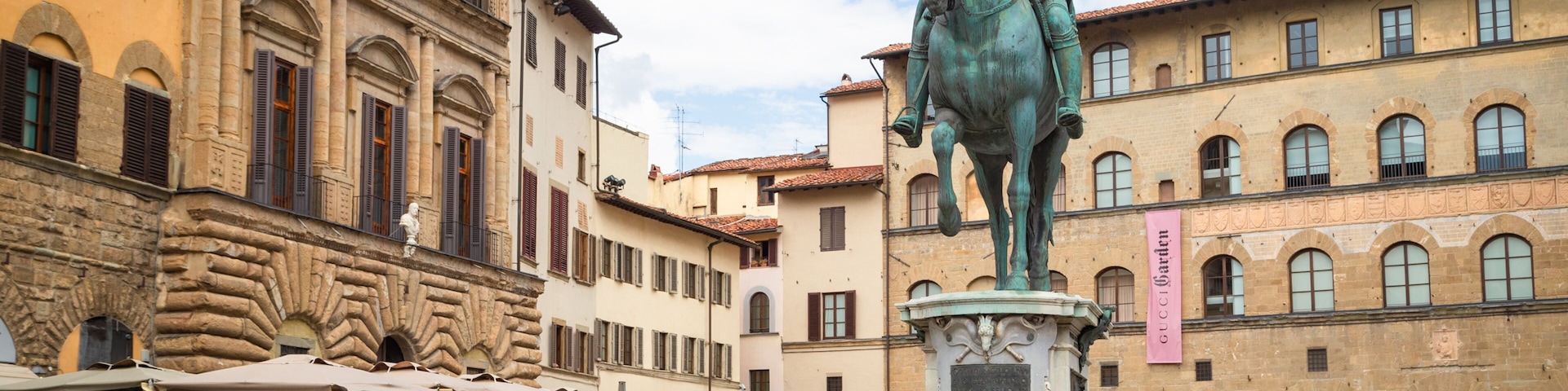 A statue of a man on horseback in a square with historic buildings and outdoor cafes.