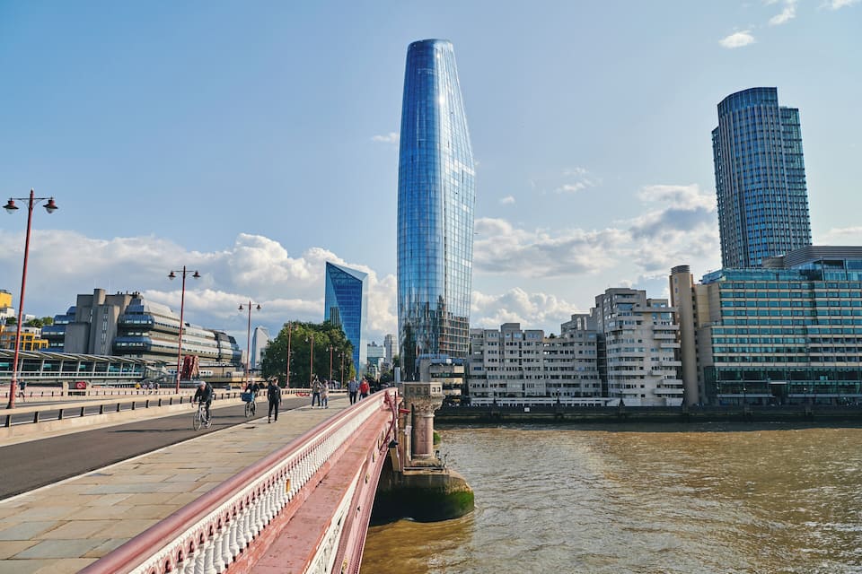 A river with a bridge, modern skyscrapers, and a pedestrian walkway.