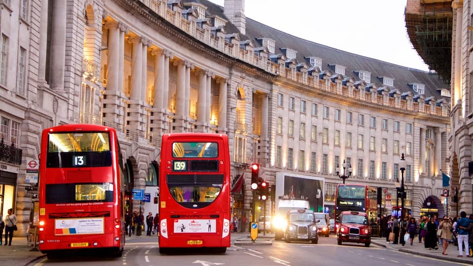Two red double-decker buses on a city street with historic buildings in the background.