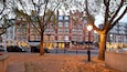 A tree-lined street with autumn leaves, a hotel, and a street lamp.