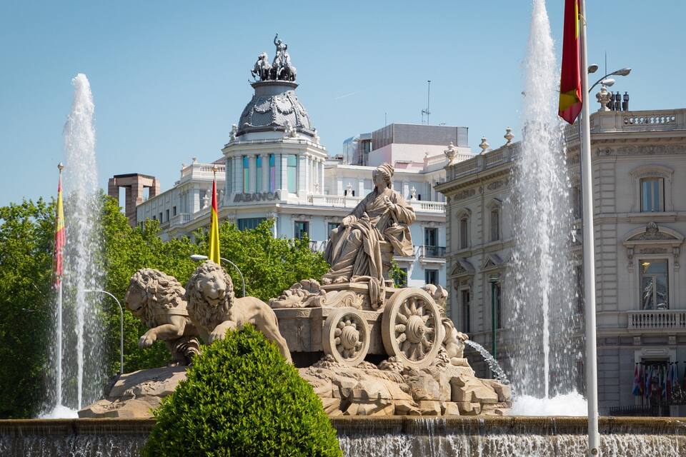 Una fuente con leones y una estatua, rodeada de edificios y banderas.