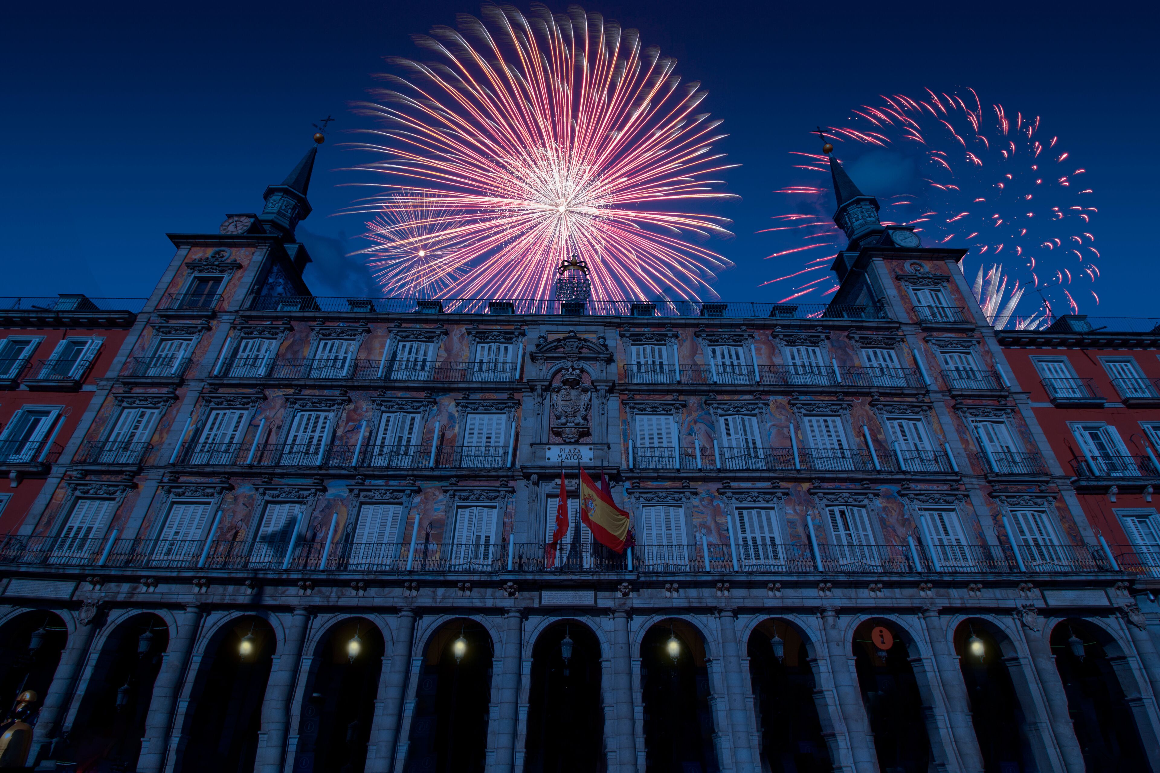 Celebratory fireworks for new year over Plaza Mayor or major square in Madrid Spain during last night of year. Christmas blue atmosphere with spain flag and lamp turn on