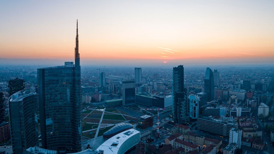 Eine Skyline mit markanten Wolkenkratzern und einem Sonnenuntergang im Hintergrund.
